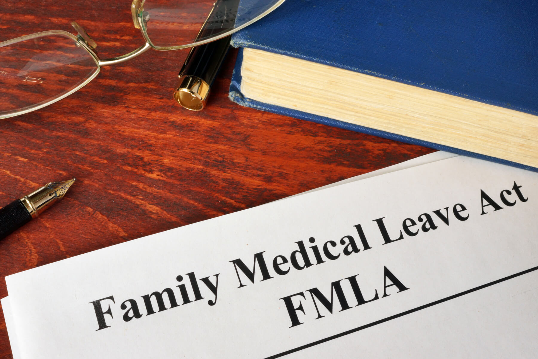 photo of a document that says FMLA Family Medical Leave Act, a pen, glasses and a book