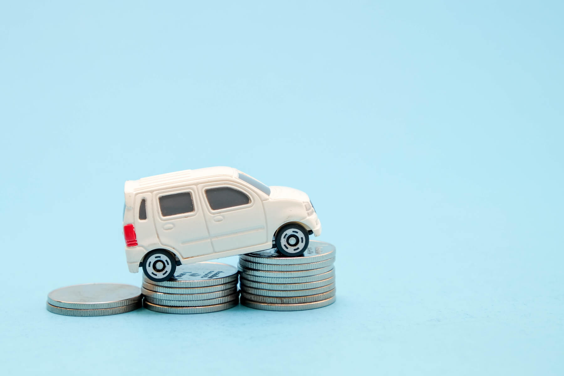 photo of a little toy car driving over coins in front of a blue background