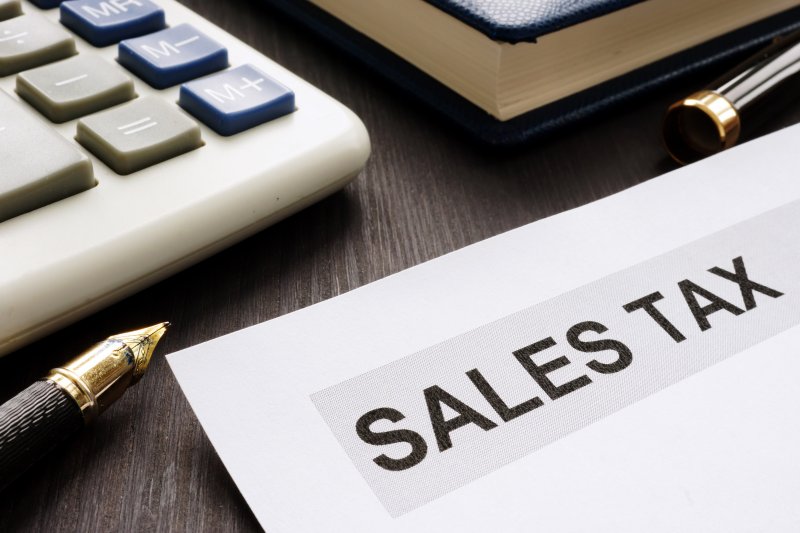 document with the word SALES TAX on it, a pen, calculator, and book