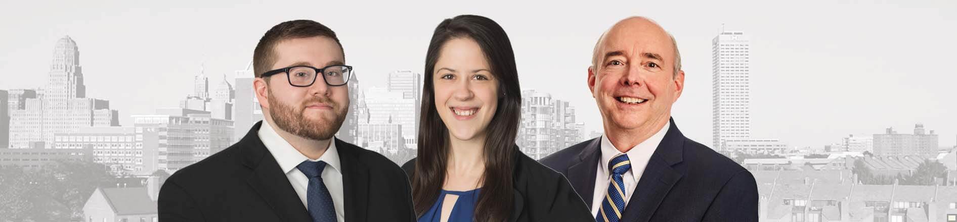 Banner photo of Buffalo NY skyline in background (grayscale) full color photo of Nicholas VanCleave, Samantha Affolter and Thomas R. Emmerling in front of the city skyline.